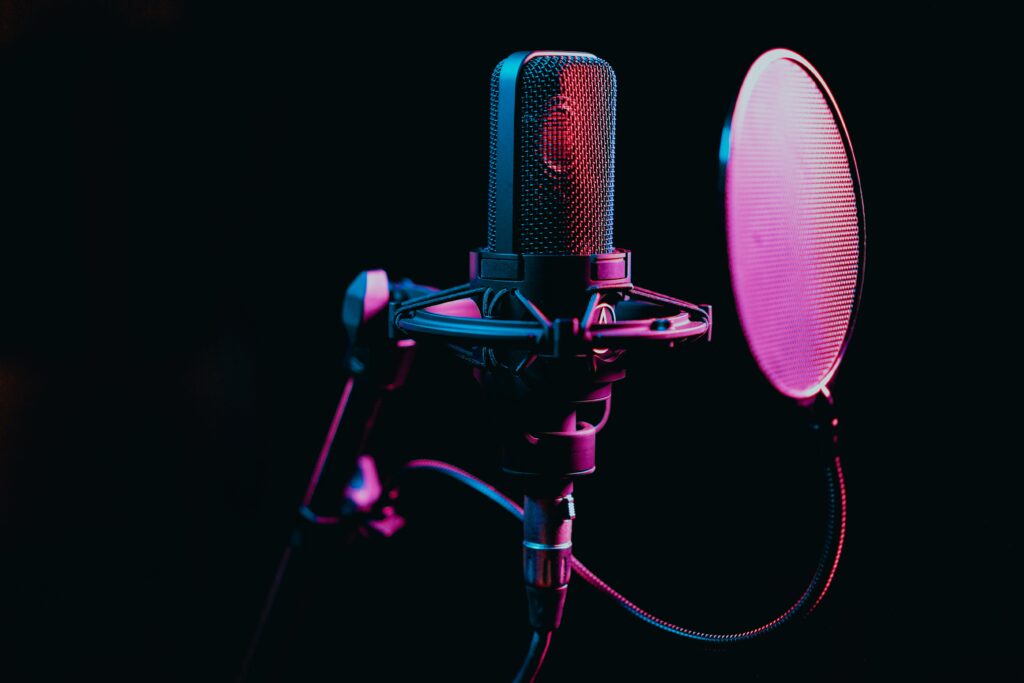 Close-up image of a condenser microphone with a pop filter in a studio setting, featuring atmospheric lighting.